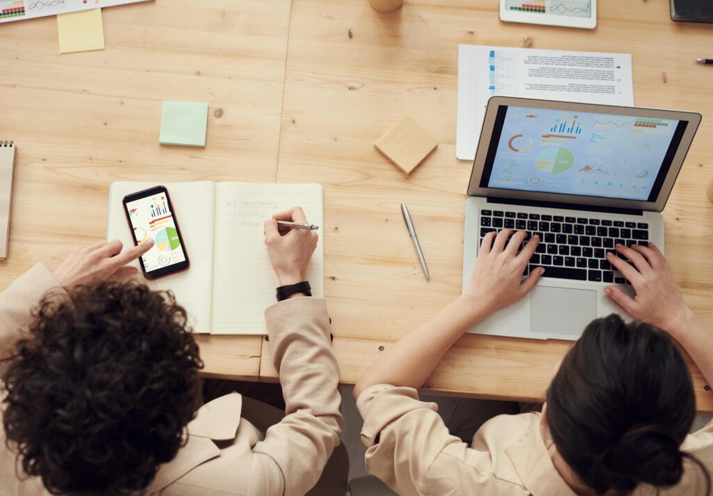 Overhead shot of two colleagues collaborating with devices and notes in a business meeting.